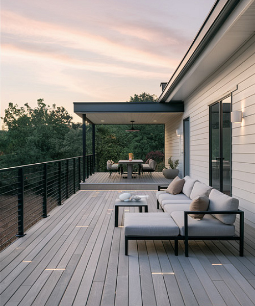 Сочетание серой террасной доски с черными ограждениями и минималистичной мебелью – дизайн, который максимально расширяет открытое пространство. А добавление встроенной подсветки создает на террасе теплую уютную атмосферу.